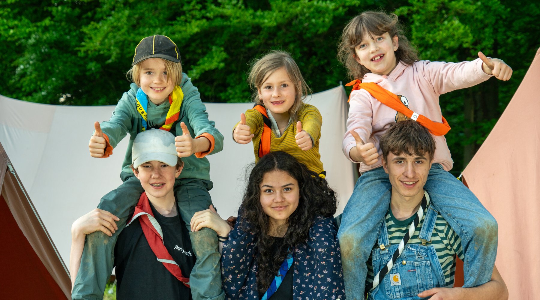 Kinder sitzen auf den Schultern ihrer Leiter*innen und strecken den Daumen hoch in die Luft. Pfadi macht Spass!